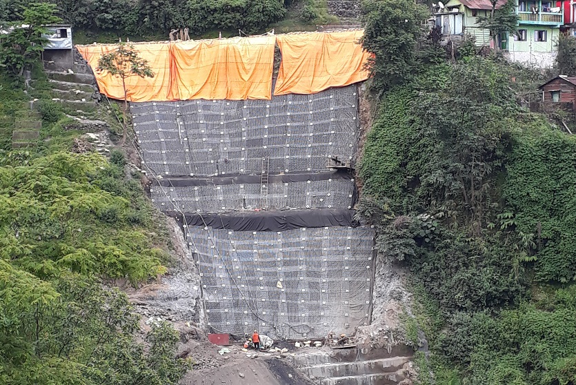 Soil nails used to secure a large draped mesh net on the side of a mountain