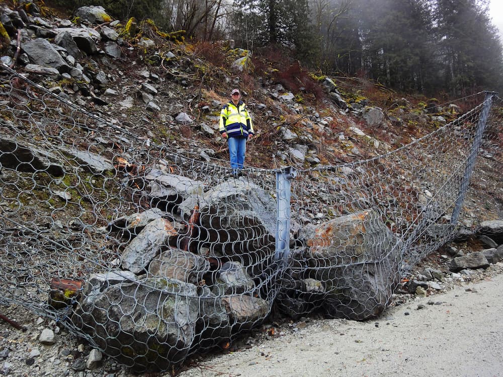 Geohazard mitigation barriers and nets support rockfall protection; man standing on fallen rocks 'caught' by rockfall protection net