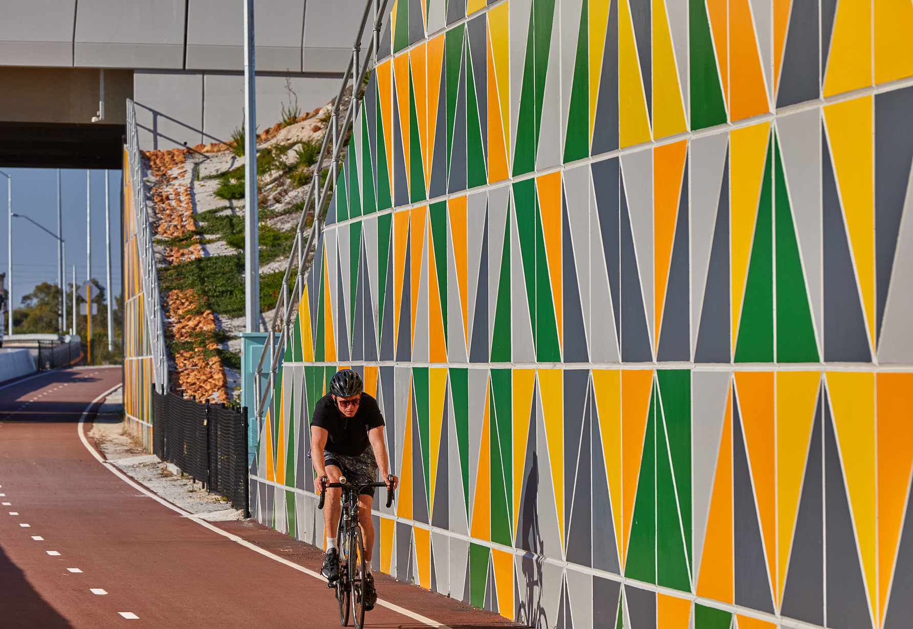 A Geoquest retaining precast concrete wall at Toking Highway, Western Australia, with a colourful modular facing panel. Bicycle rider riding on the cycle path in front of the wall.