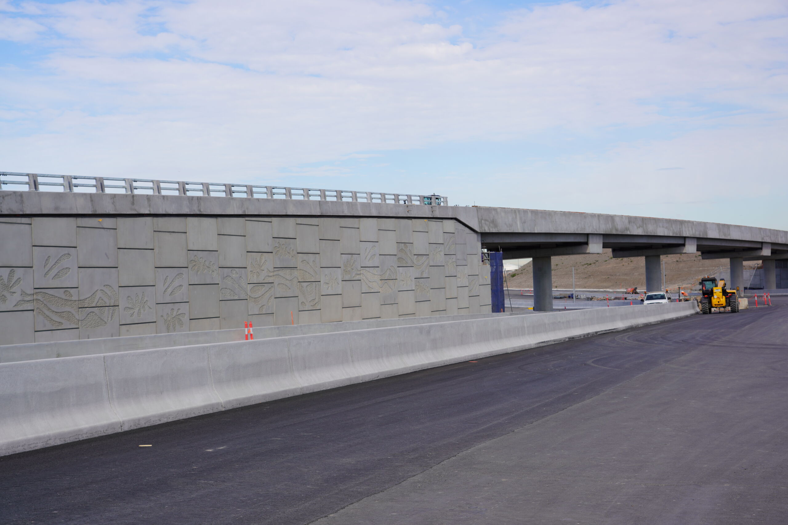 A reinforced earth wall (MSE wall) supporting a road bridge at the Sydney Gateway project, New South Wales, which has pre cast concrete facing panels with decorative elements engraved.